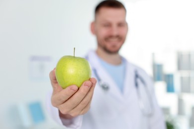 Photo of Nutritionist with green apple and stethoscope in clinic, selective focus