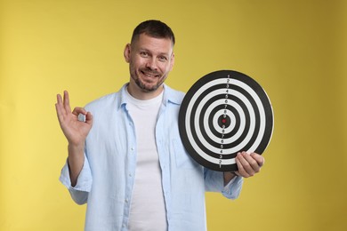 Photo of Targeting. Man with dart board showing ok gesture on yellow background