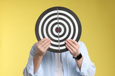 Photo of Targeting. Man with dart board on yellow background