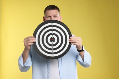 Photo of Targeting. Man with dart board on yellow background