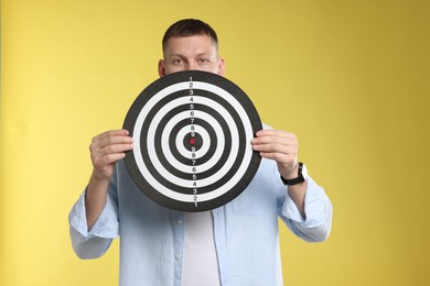 Photo of Targeting. Man with dart board on yellow background