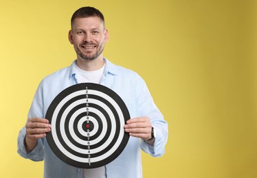 Photo of Targeting. Man with dart board on yellow background, space for text