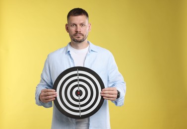 Photo of Targeting. Man with dart board on yellow background