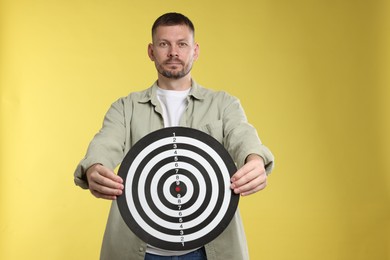 Photo of Targeting. Man with dart board on yellow background