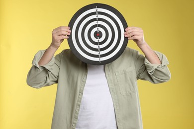 Photo of Targeting. Man with dart board on yellow background