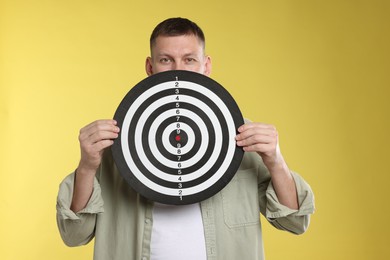 Photo of Targeting. Man with dart board on yellow background