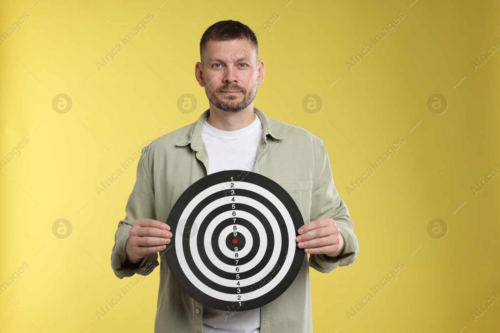 Targeting. Man with dart board on yellow background Photo of Targeting. Man with dart board on yellow background