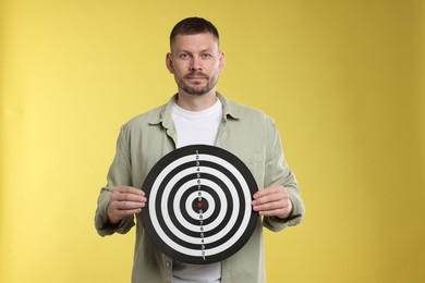 Photo of Targeting. Man with dart board on yellow background