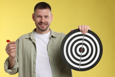 Photo of Targeting. Man with dart board and arrow on yellow background