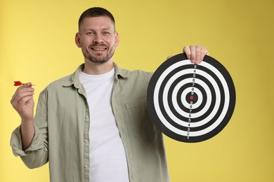 Photo of Targeting. Man with dart board and arrow on yellow background