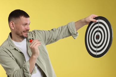Photo of Targeting. Man with dart board and arrow on yellow background