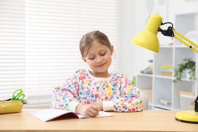 Photo of Little girl doing homework at table indoors