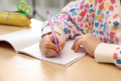 Photo of Little girl doing homework at table indoors, closeup