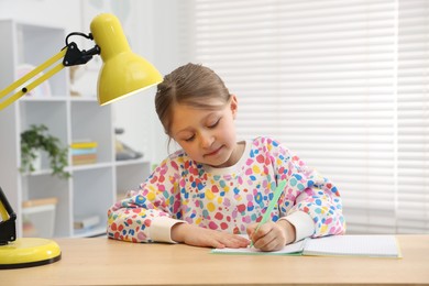 Photo of Little girl doing homework at table indoors