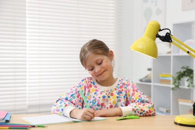 Photo of Little girl doing homework at table indoors