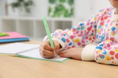 Photo of Little girl doing homework at table indoors, closeup