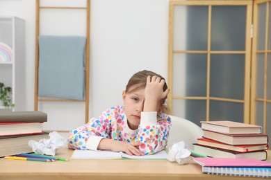 Photo of Tired little girl doing homework at table indoors