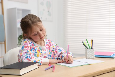 Photo of Little girl doing homework at table indoors