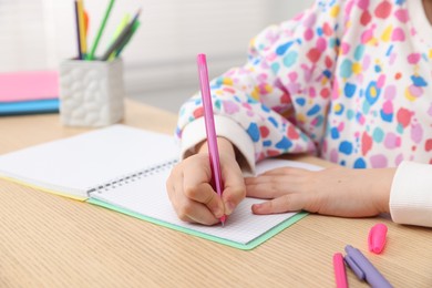Photo of Little girl doing homework at table indoors, closeup