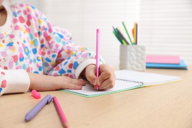 Photo of Little girl doing homework at table indoors, closeup