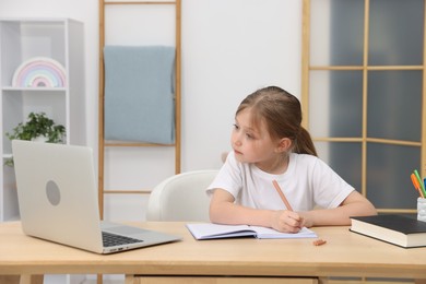 Photo of Little girl doing homework at table indoors