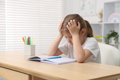 Photo of Tired little girl doing homework at table indoors