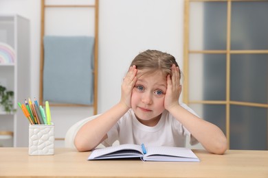 Photo of Tired little girl doing homework at table indoors