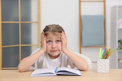 Photo of Tired little girl doing homework at table indoors