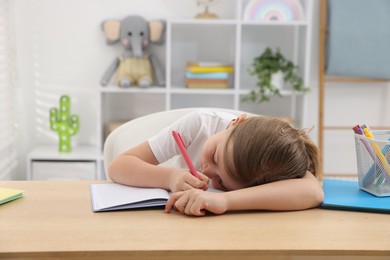 Photo of Tired little girl doing homework at table indoors