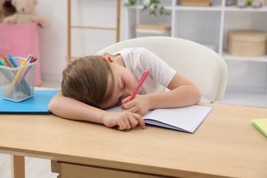 Photo of Tired little girl doing homework at table indoors
