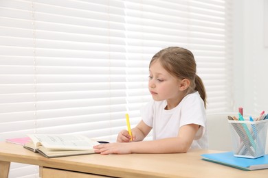 Photo of Little girl doing homework at table indoors
