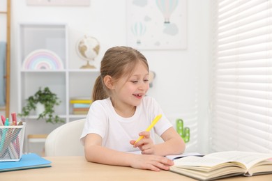 Photo of Little girl doing homework at table indoors
