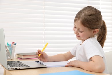 Photo of Little girl doing homework at table indoors