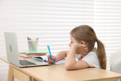 Photo of Tired little girl doing homework at table indoors