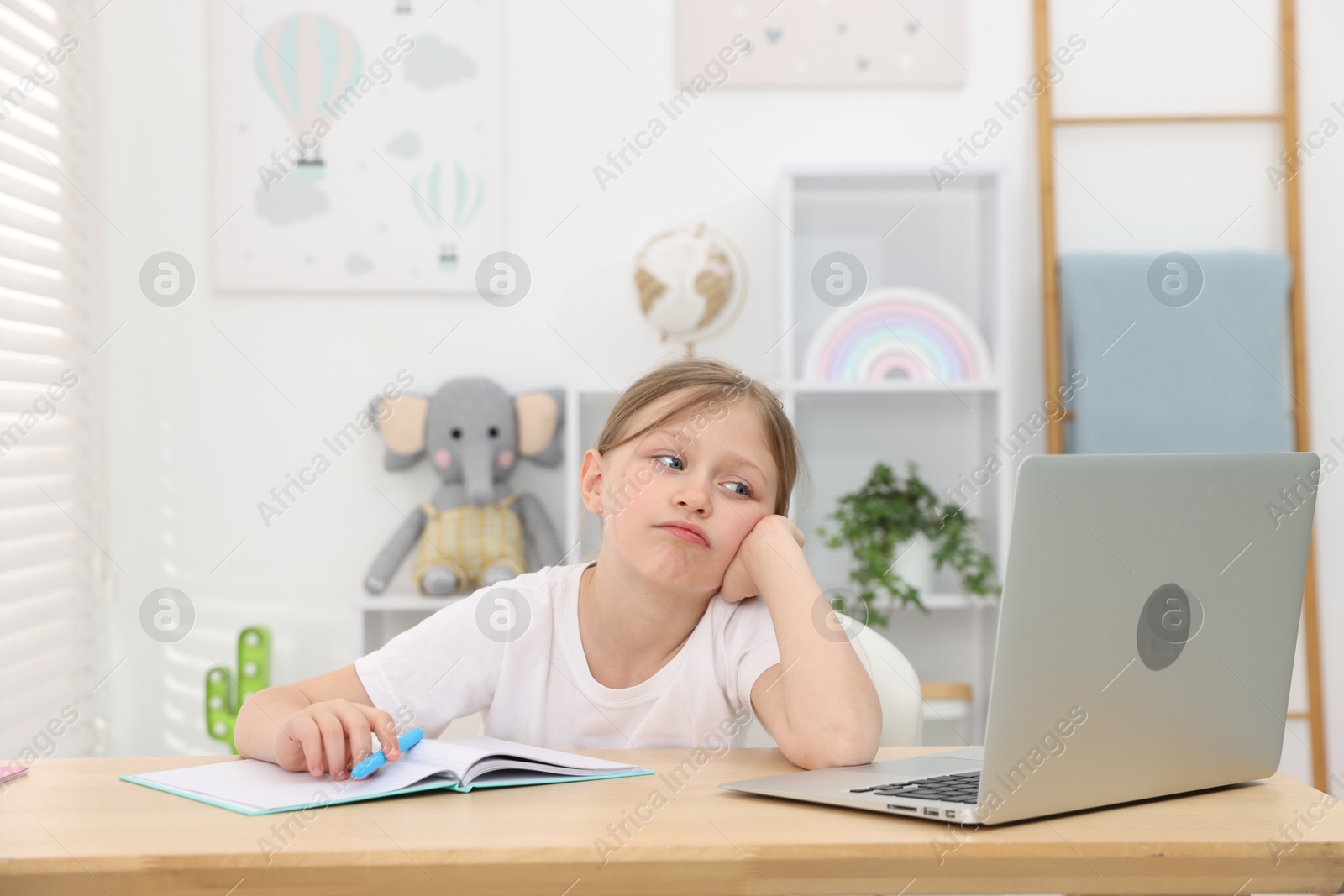 Photo of Tired little girl doing homework at table indoors