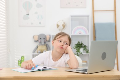 Photo of Tired little girl doing homework at table indoors