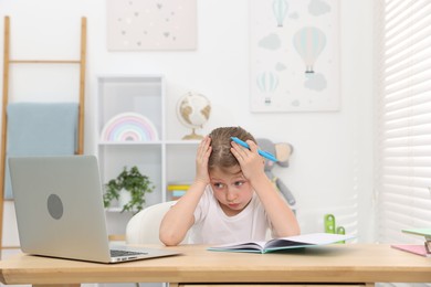 Photo of Tired little girl doing homework at table indoors
