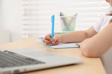 Photo of Little girl doing homework at table indoors, closeup