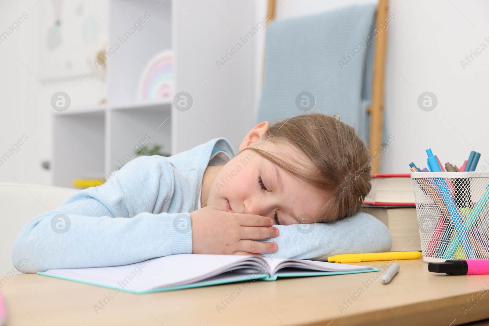 Photo of Tired little girl doing homework at table indoors