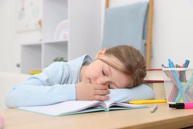 Photo of Tired little girl doing homework at table indoors