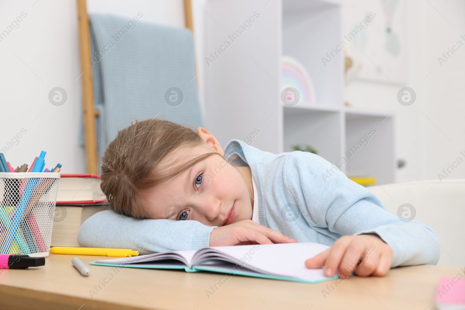 Photo of Tired little girl doing homework at table indoors