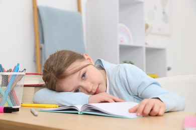 Photo of Tired little girl doing homework at table indoors
