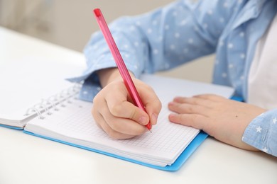 Photo of Little girl doing homework at table indoors, closeup