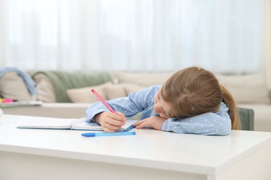 Photo of Tired little girl doing homework at table indoors