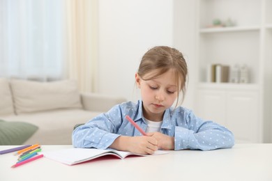 Photo of Little girl doing homework at table indoors