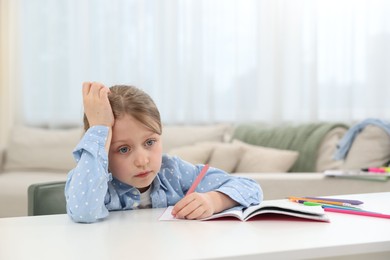 Photo of Tired little girl doing homework at table indoors