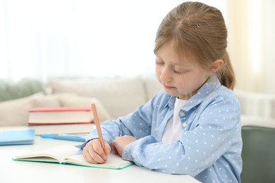 Photo of Little girl doing homework at table indoors