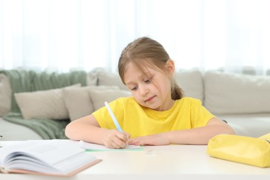 Photo of Little girl doing homework at table indoors