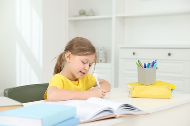 Photo of Little girl doing homework at table indoors