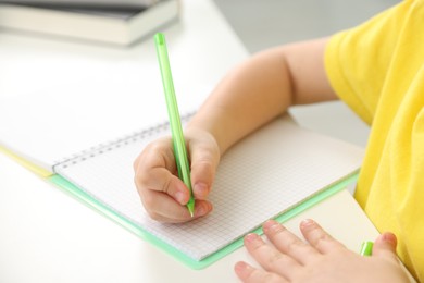 Photo of Little girl doing homework at table indoors, closeup